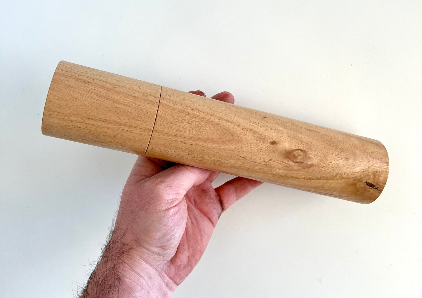 Mans hand holding single straight cylindrical Blackbutt timber grinder