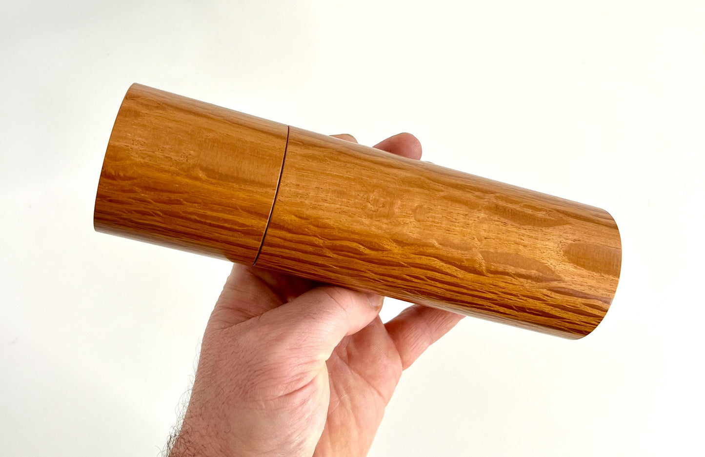Mans hand holding single straight cylindrical Sheoak timber grinder