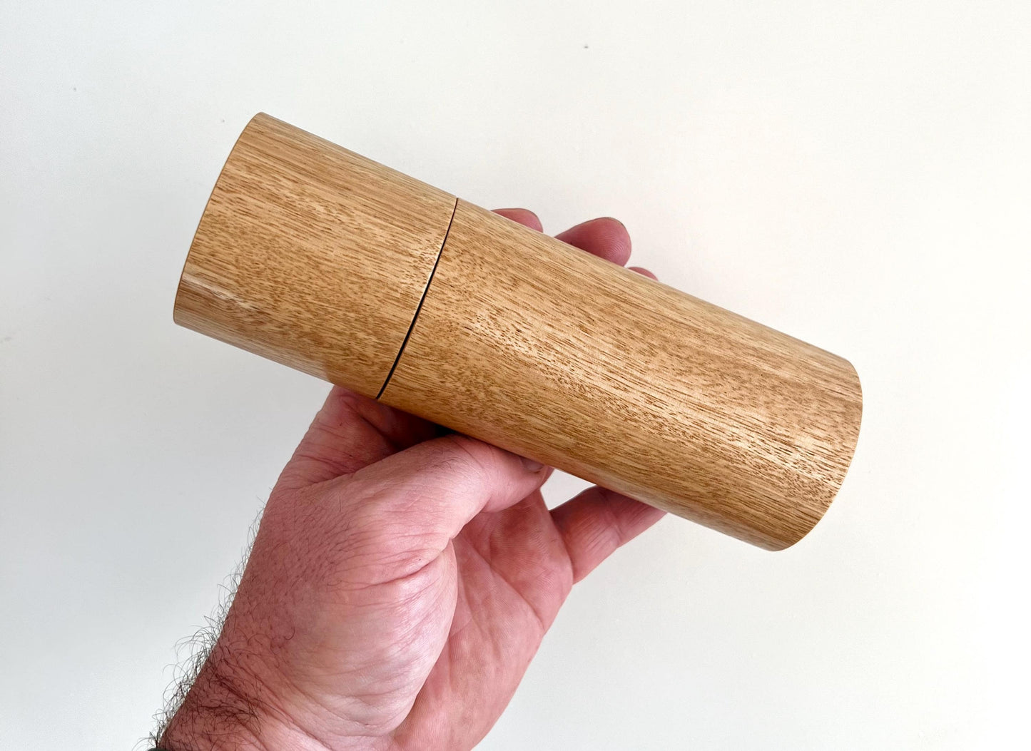 Mans hand holding single straight cylindrical Blackbutt timber grinder