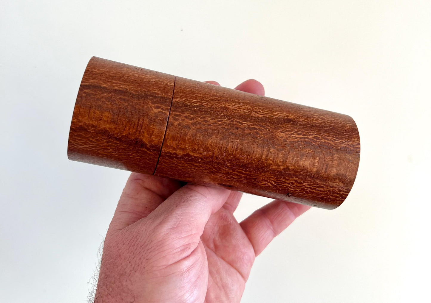 Mans hand holding single straight cylindrical Banksia timber grinder