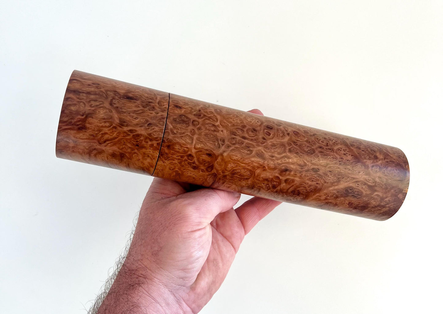 Mans hand holding single straight cylindrical Blackbutt burl timber grinder