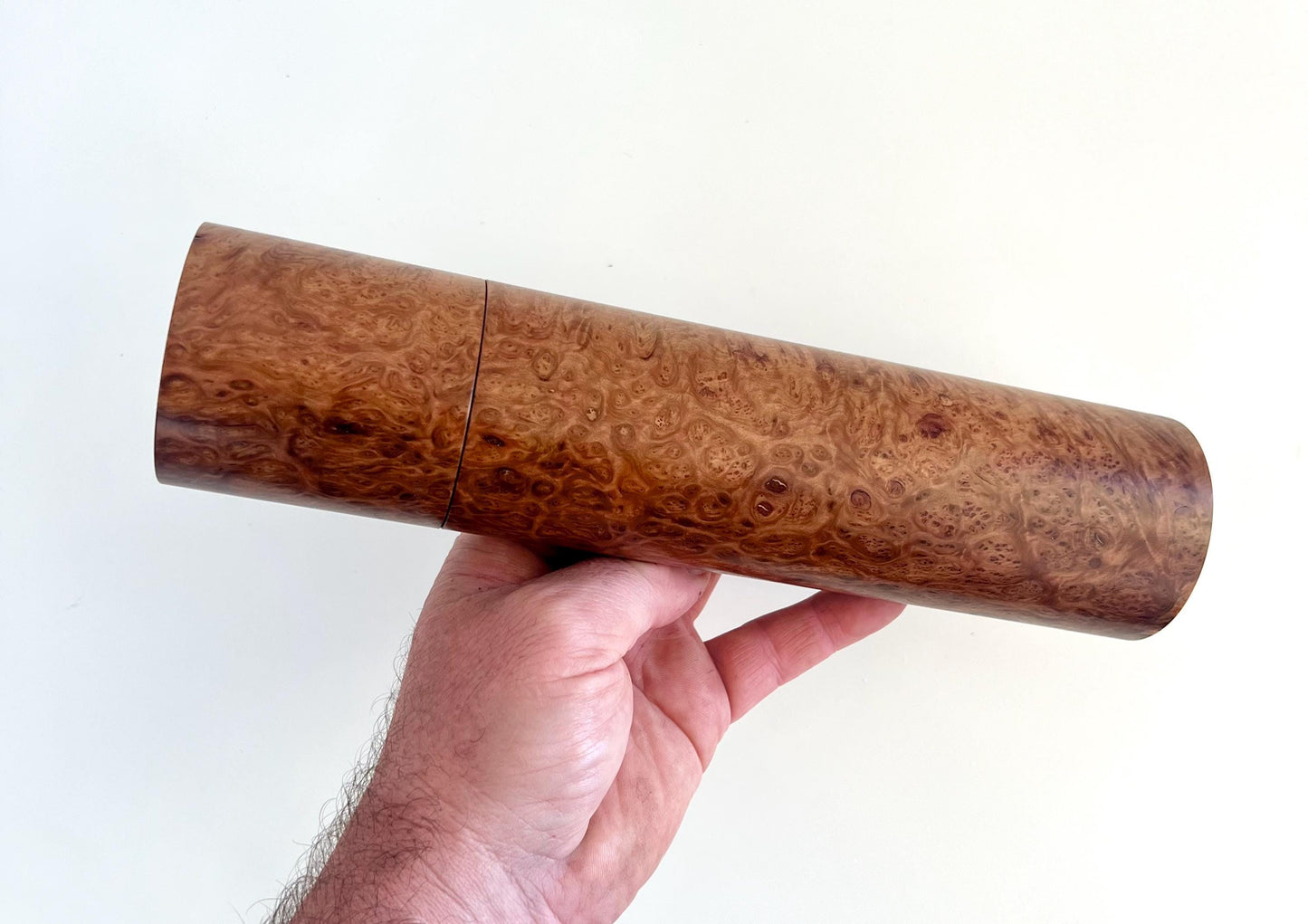 Mans hand holding single straight cylindrical Blackbutt burl timber grinder
