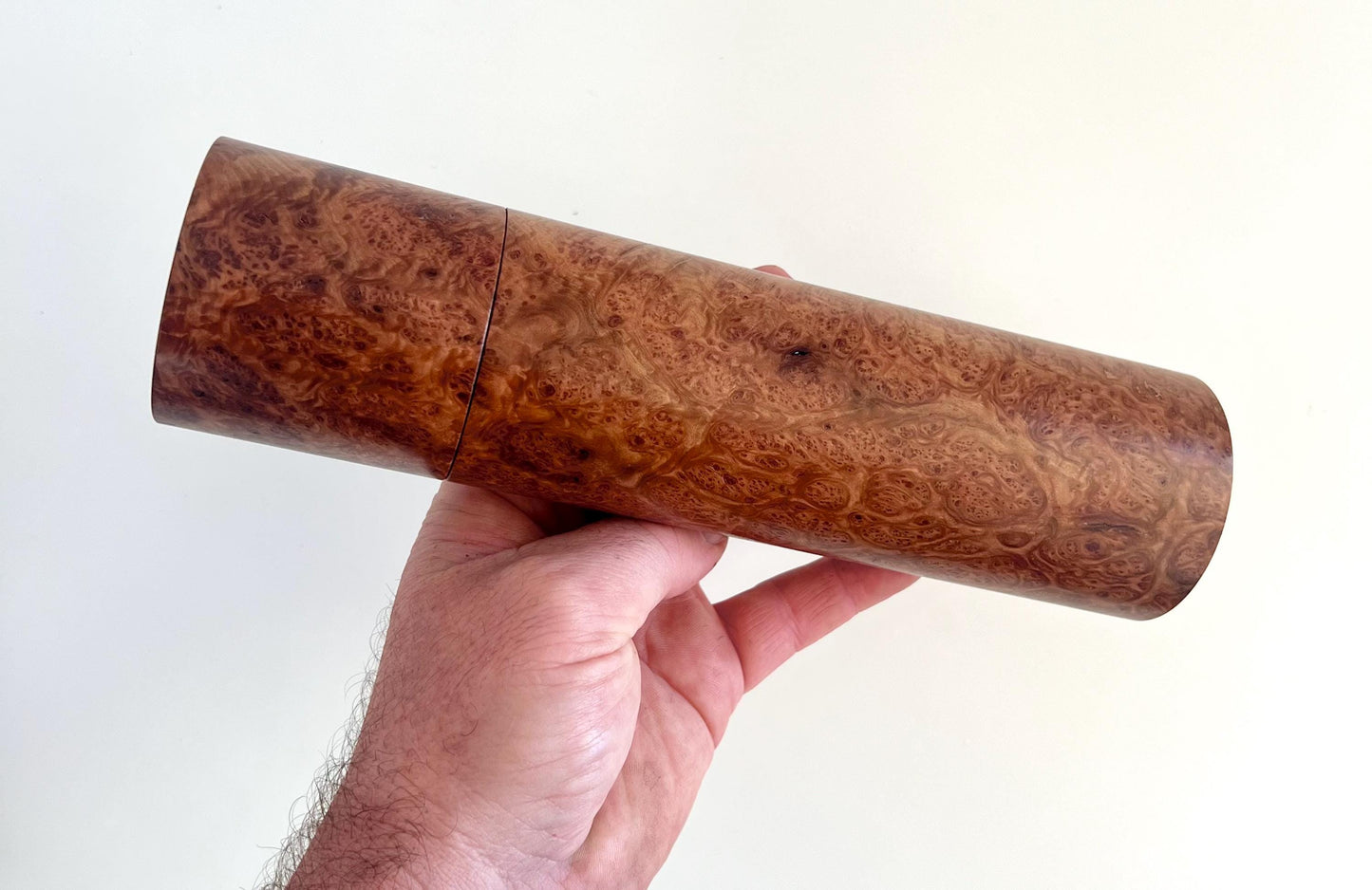 Mans hand holding single straight cylindrical Blackbutt burl timber grinder