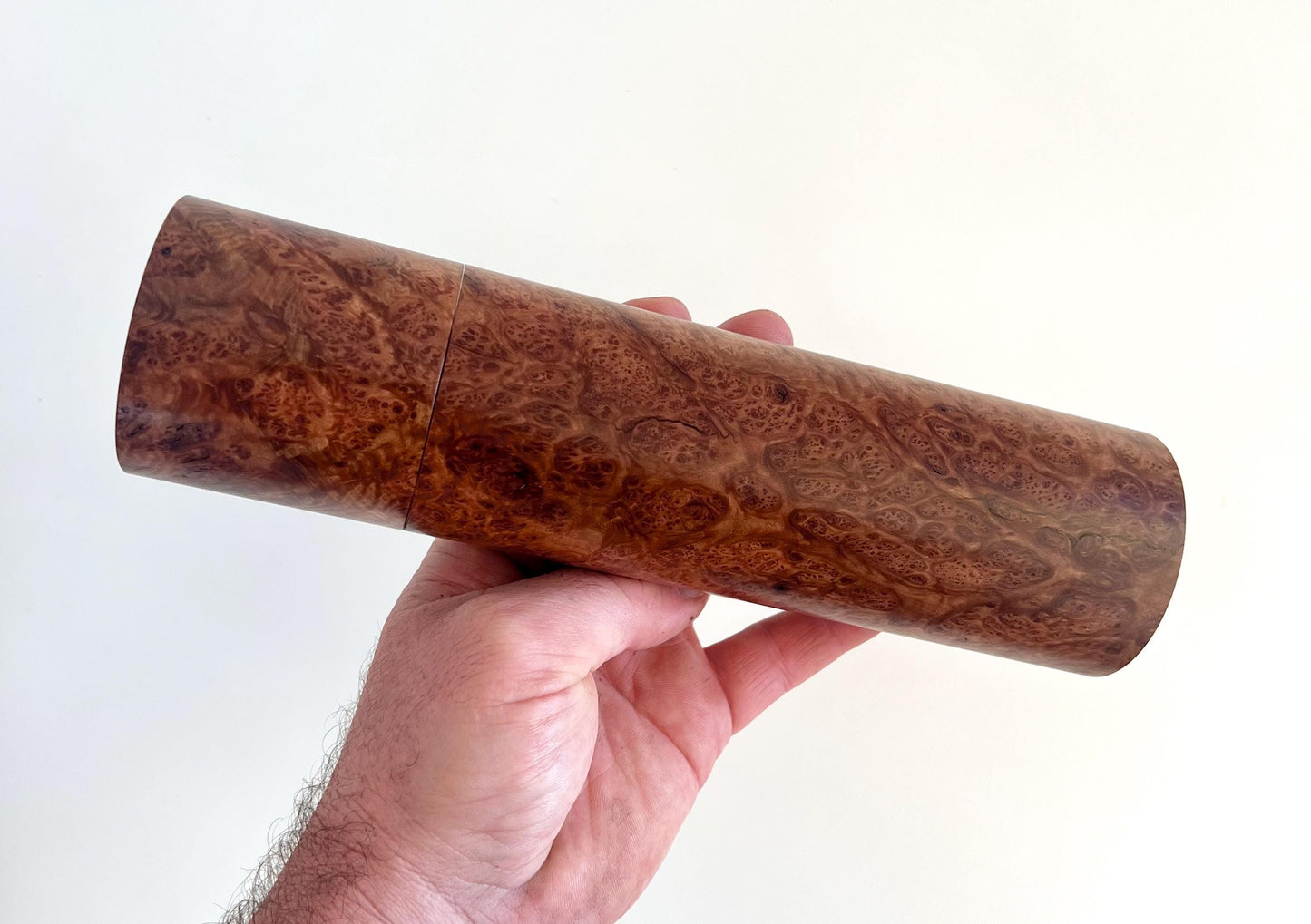 Mans hand holding single straight cylindrical Blackbutt burl timber grinder