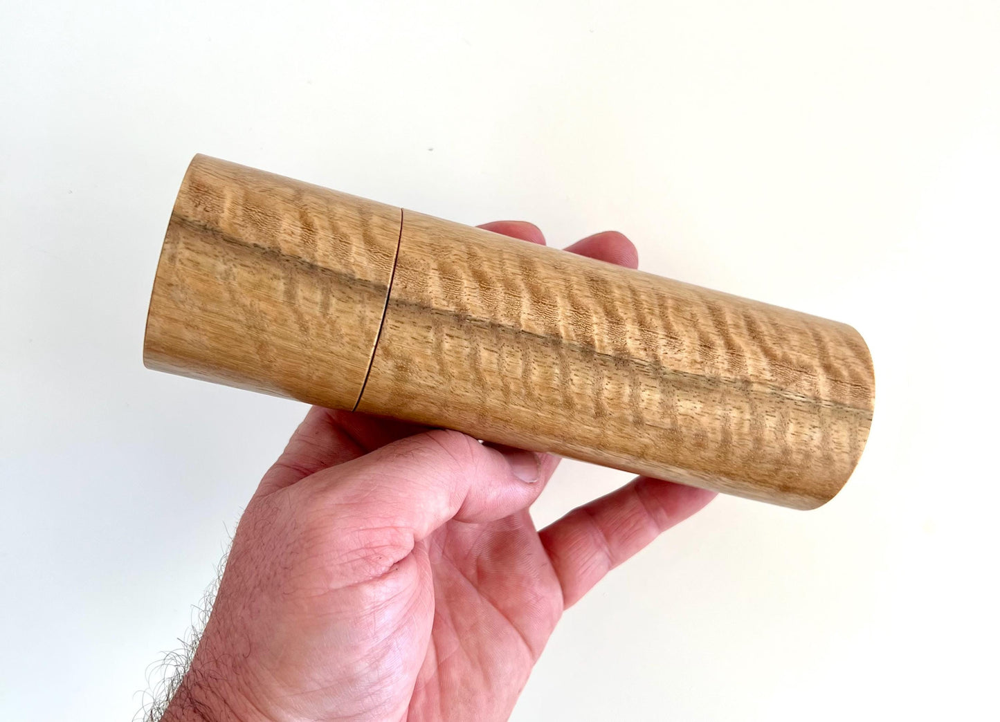 Mans hand holding single straight cylindrical Marri timber grinder