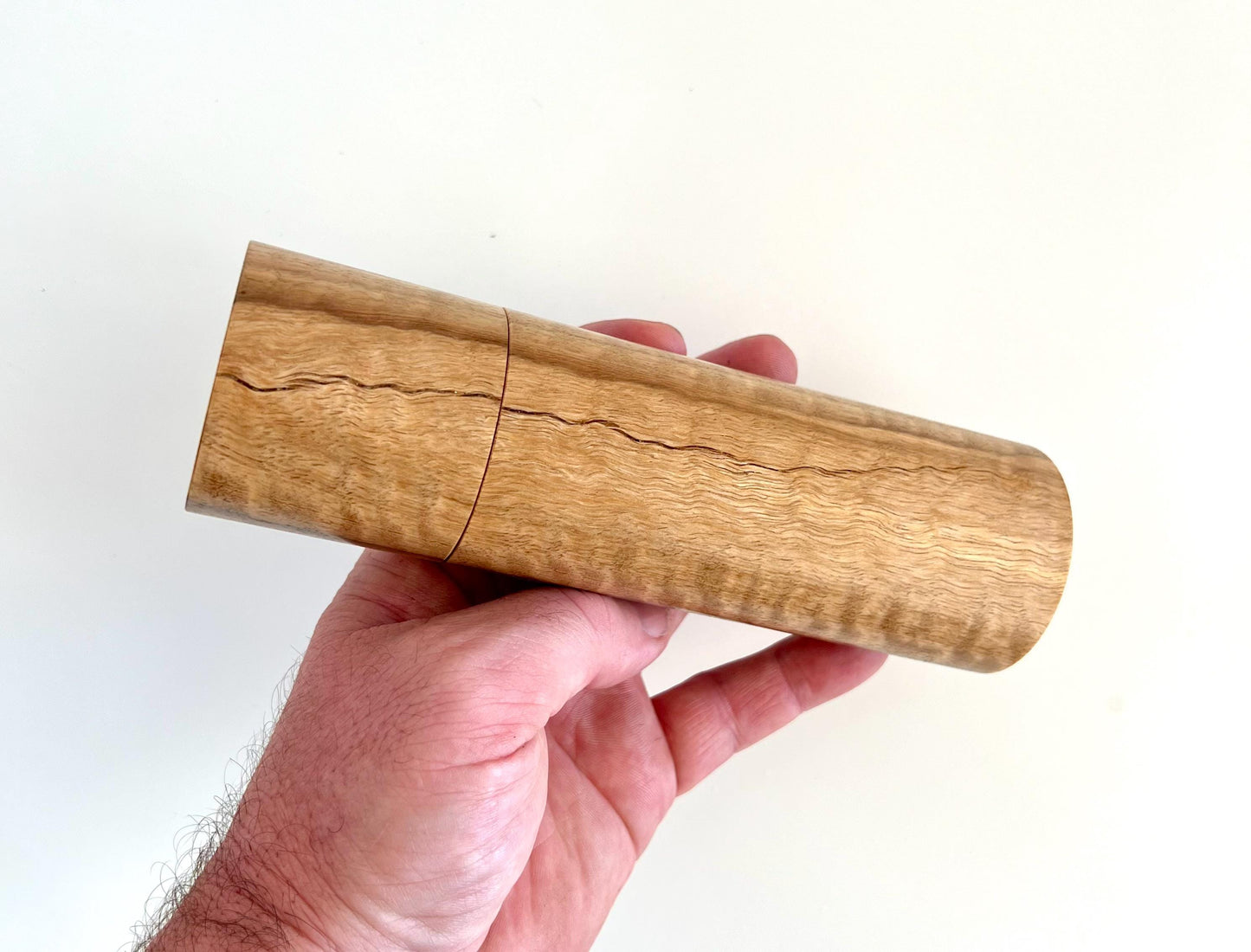 Mans hand holding single straight cylindrical Marri timber grinder