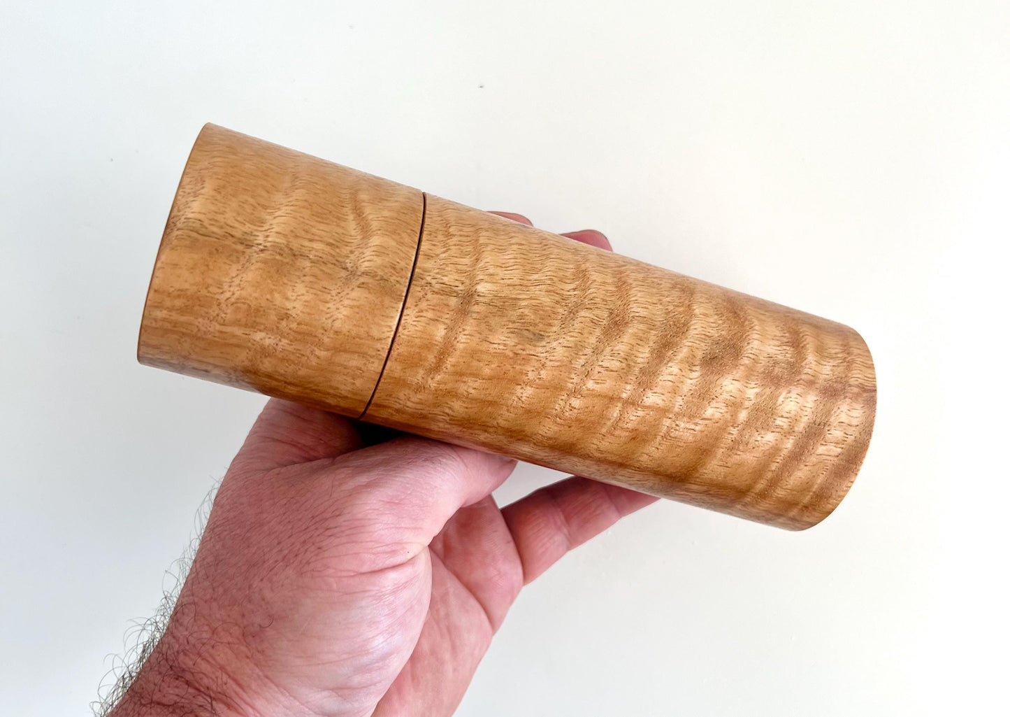 Mans hand holding single straight cylindrical Marri timber grinder
