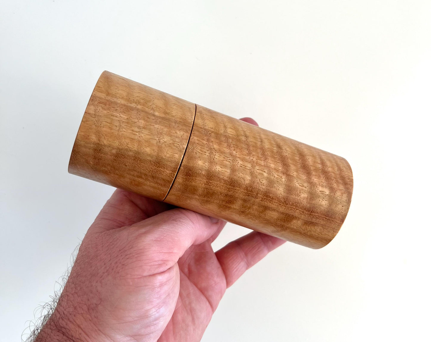 Mans hand holding single straight cylindrical Marri timber grinder