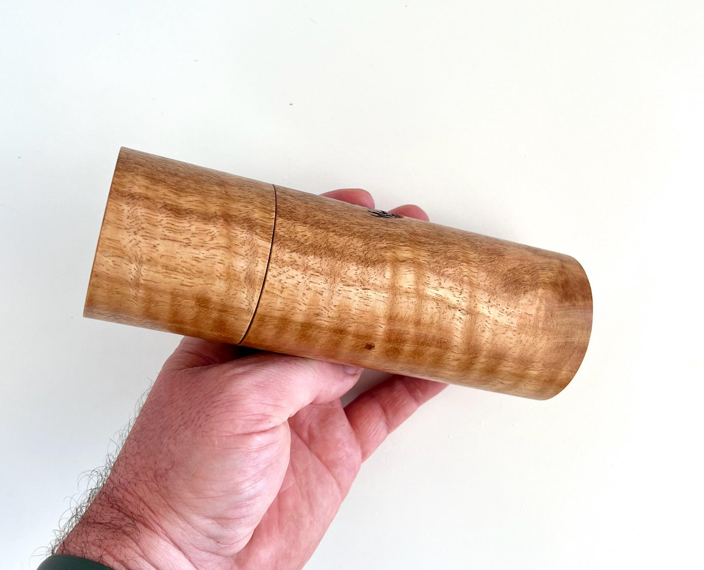 Mans hand holding single straight cylindrical Marri timber grinder