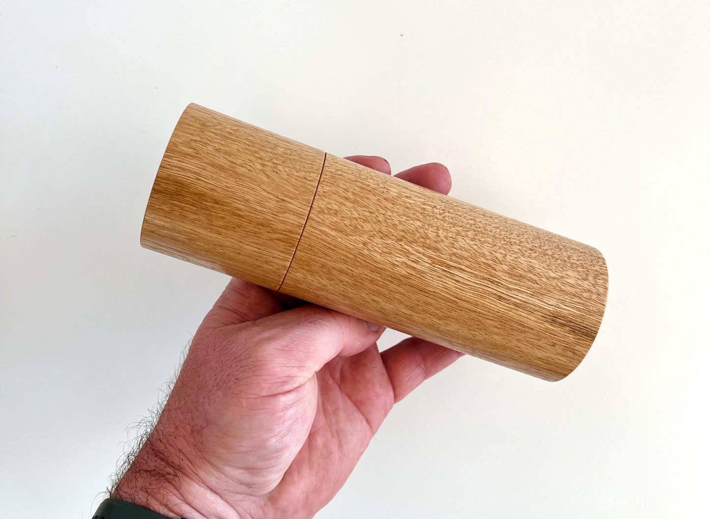 Mans hand holding single straight cylindrical Blackbutt timber grinder