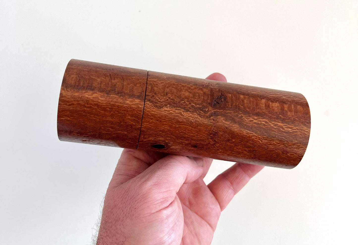 Mans hand holding single straight cylindrical Banksia timber grinder