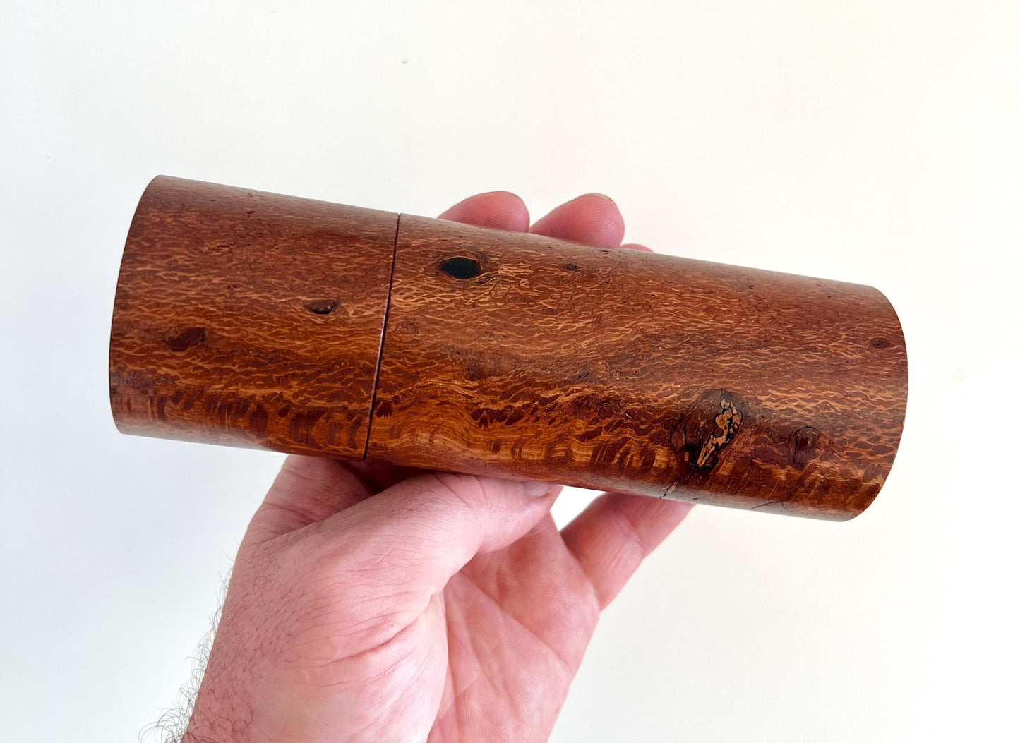 Mans hand holding single straight cylindrical Banksia timber grinder