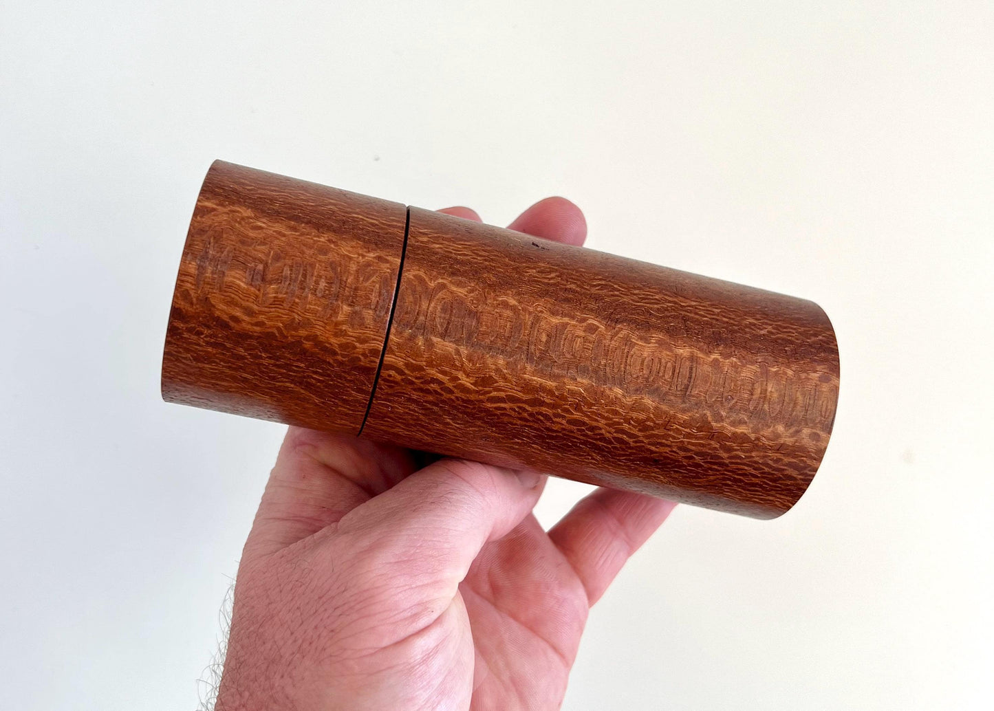Mans hand holding single straight cylindrical Banksia timber grinder