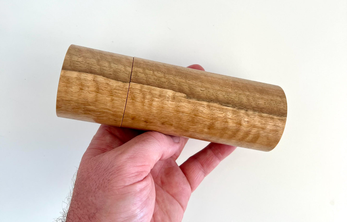 Mans hand holding single straight cylindrical Marri timber grinder