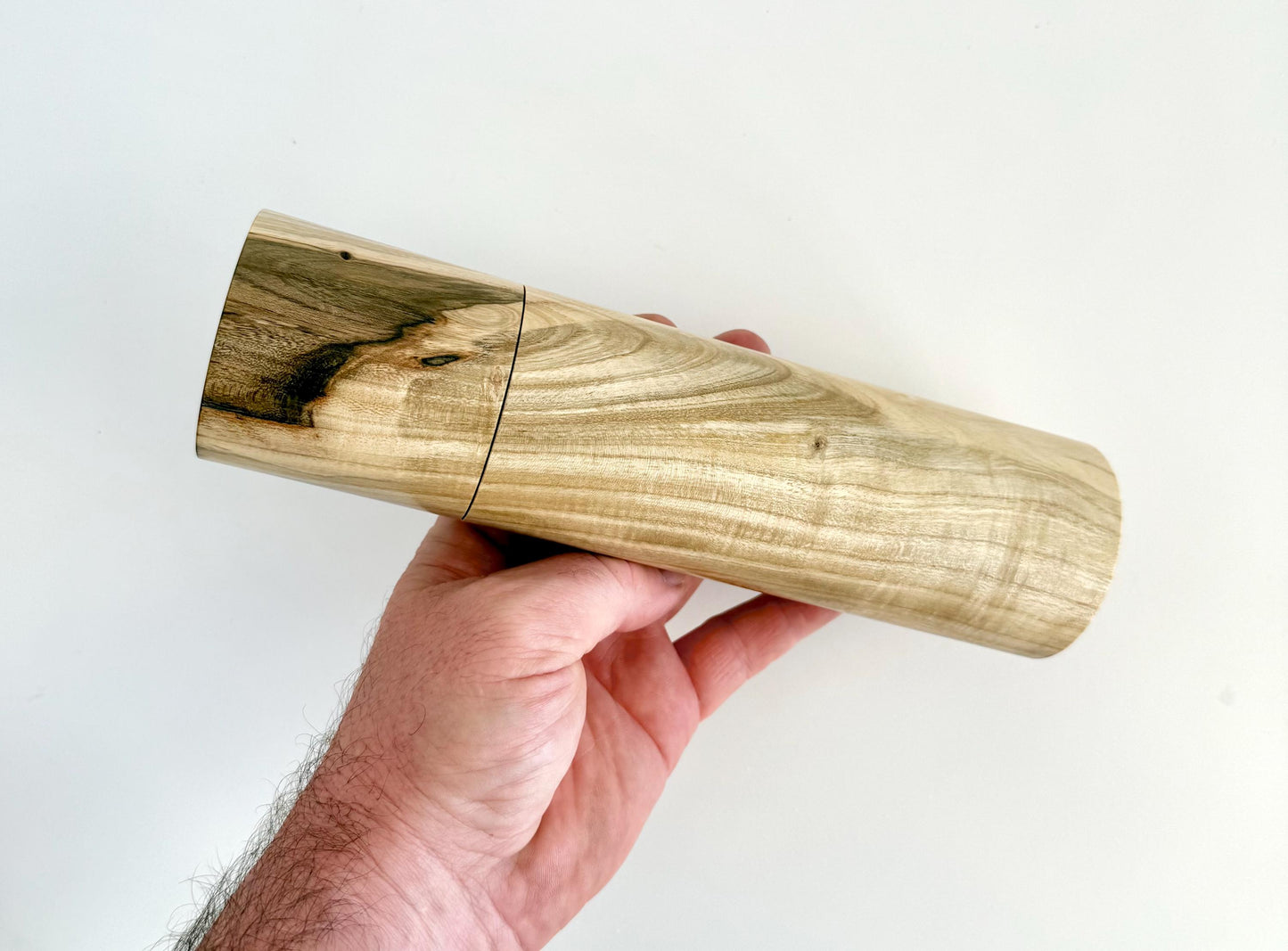 Mans hand holding single straight cylindrical Pistachio timber grinder