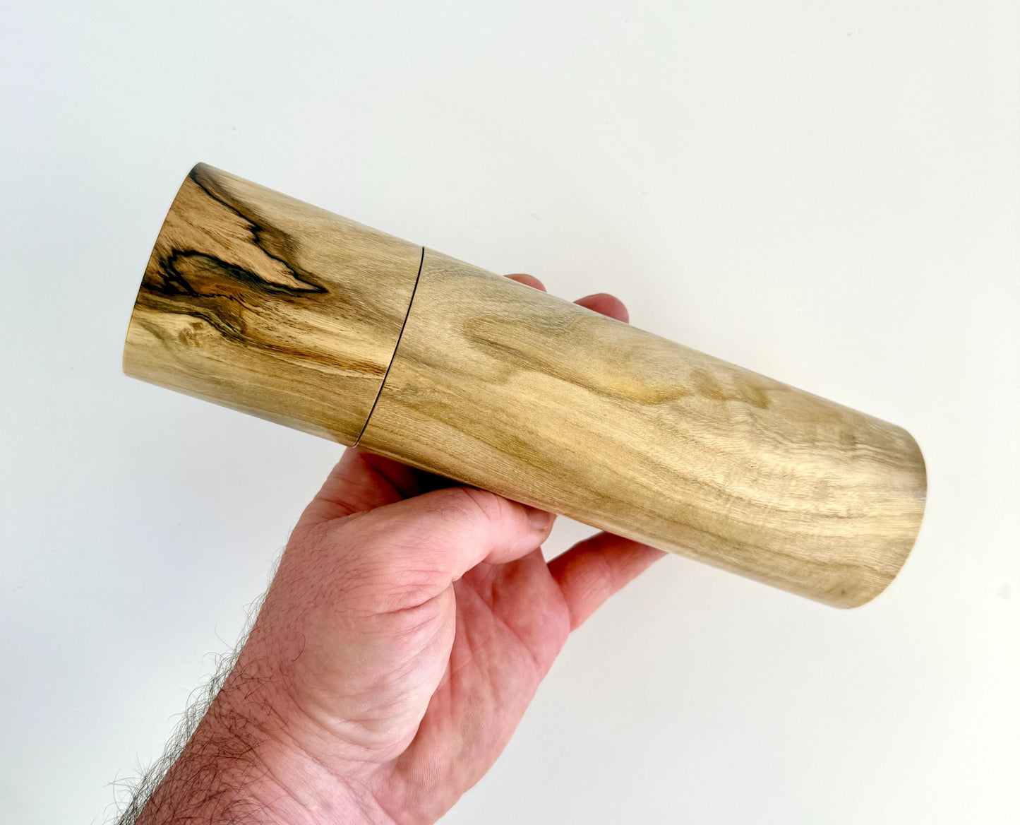 Mans hand holding single straight cylindrical Pistachio timber grinder
