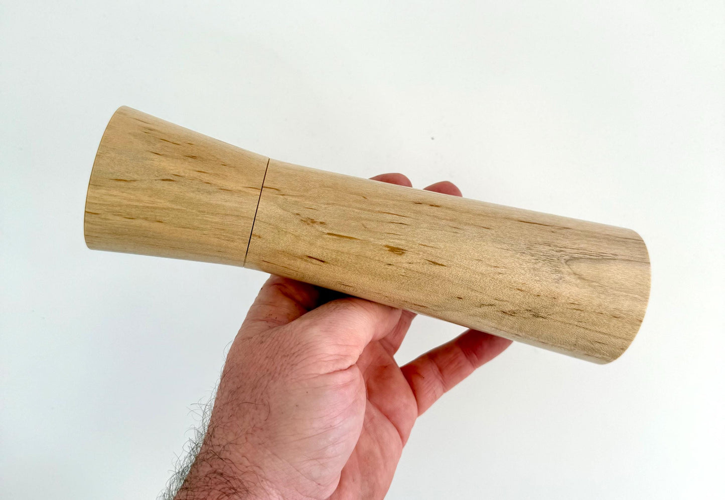 Mans hand holding single straight cylindrical Maple timber grinder