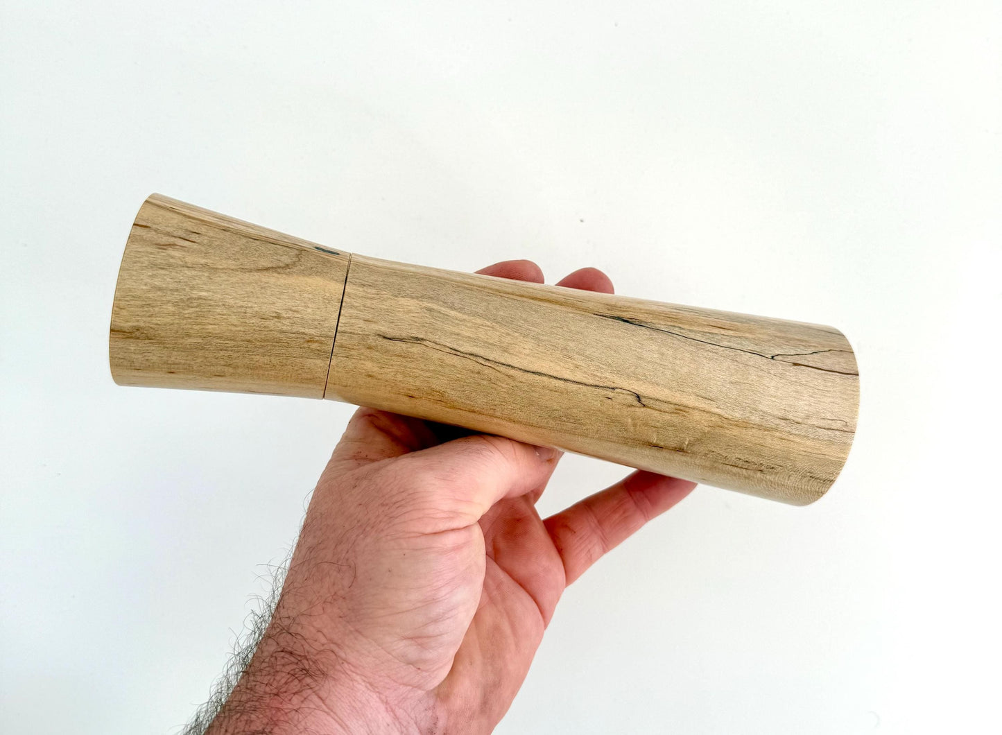 Mans hand holding single straight cylindrical Maple timber grinder