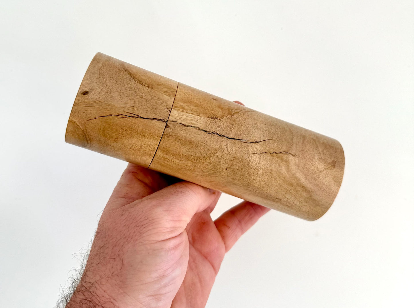 Mans hand holding single straight cylindrical Lemon scented gum timber grinder