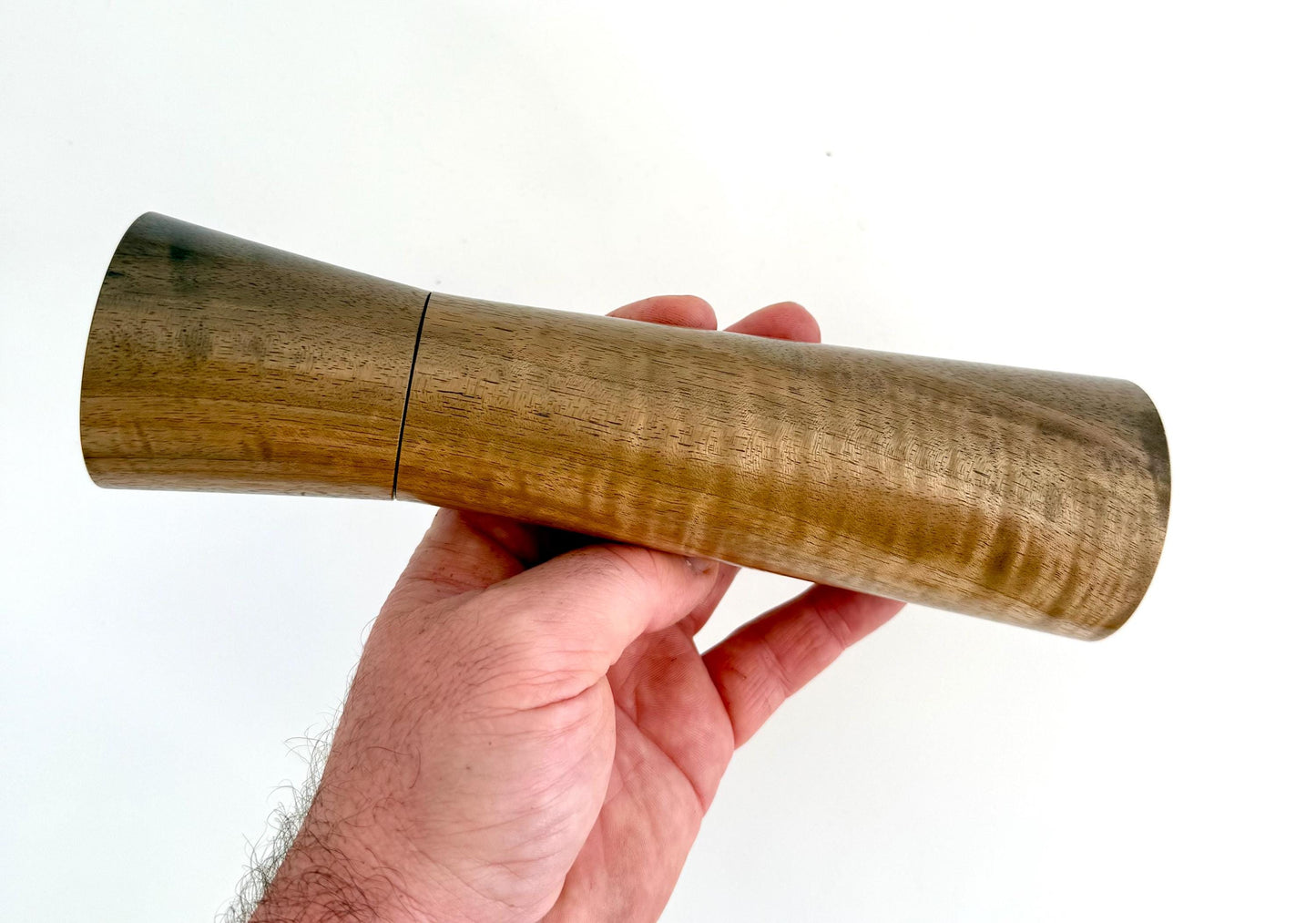 Mans hand holding single straight cylindrical Walnut timber grinder