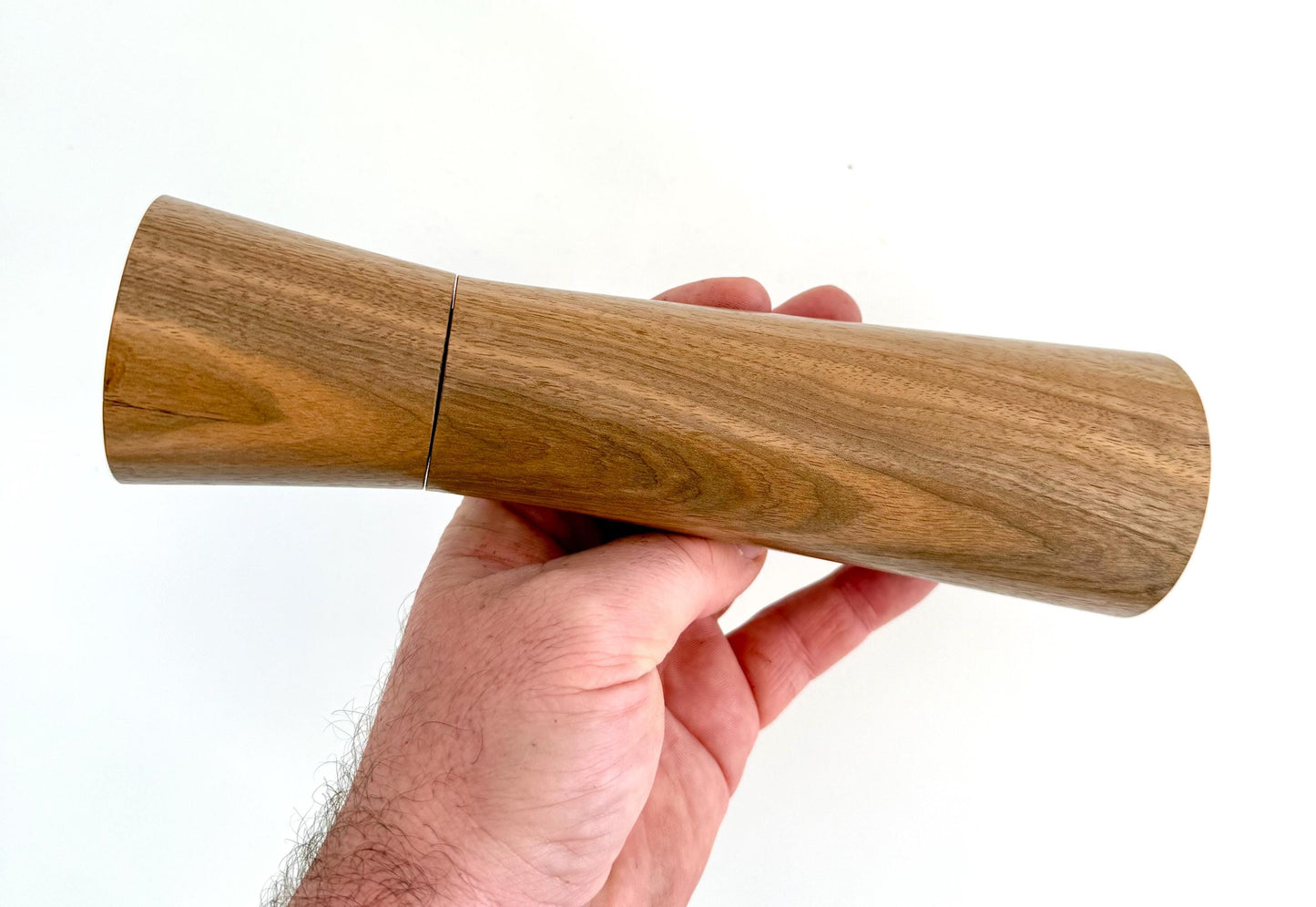Mans hand holding single straight cylindrical Walnut timber grinder