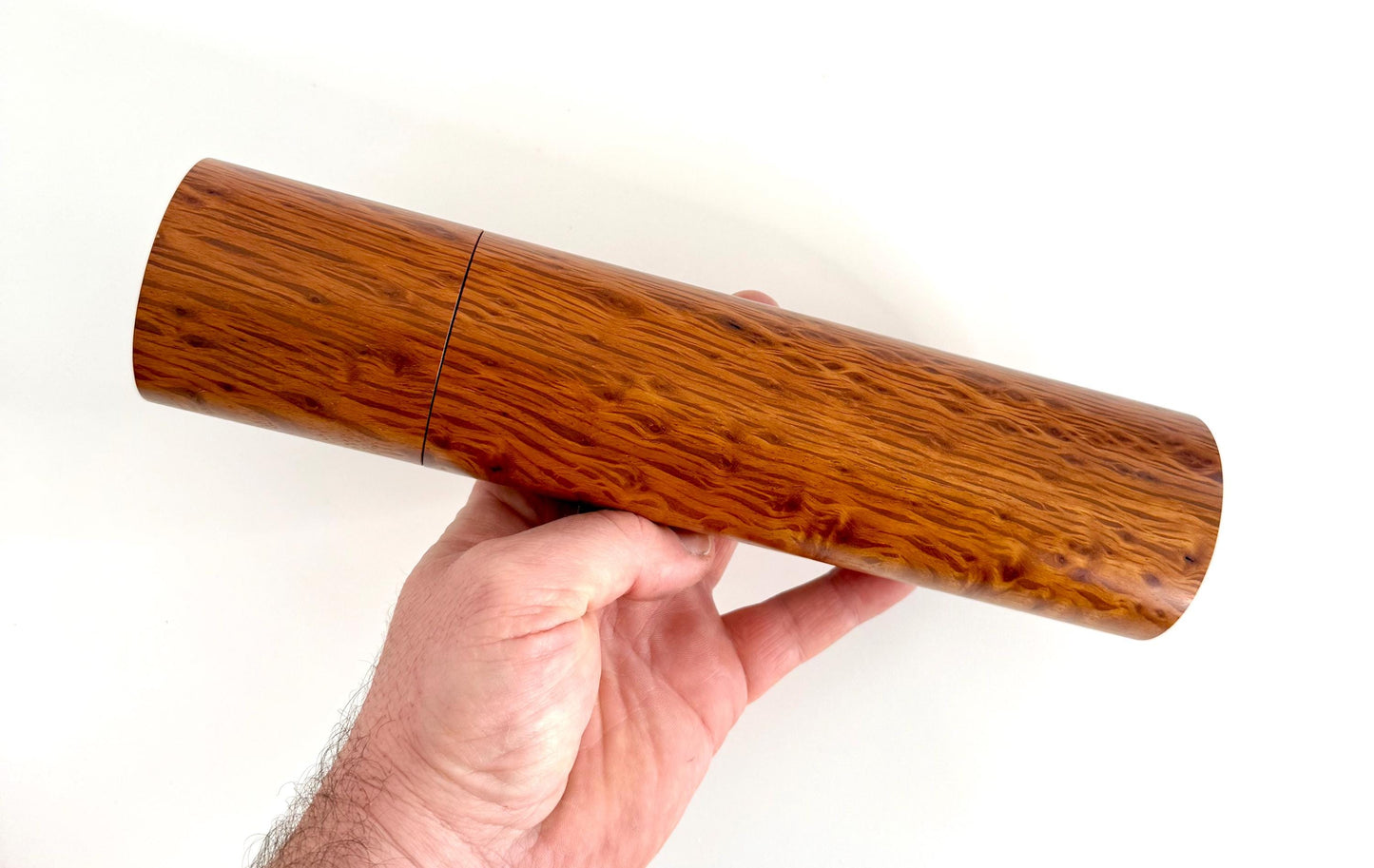 Mans hand holding single straight cylindrical Sheoak timber grinder