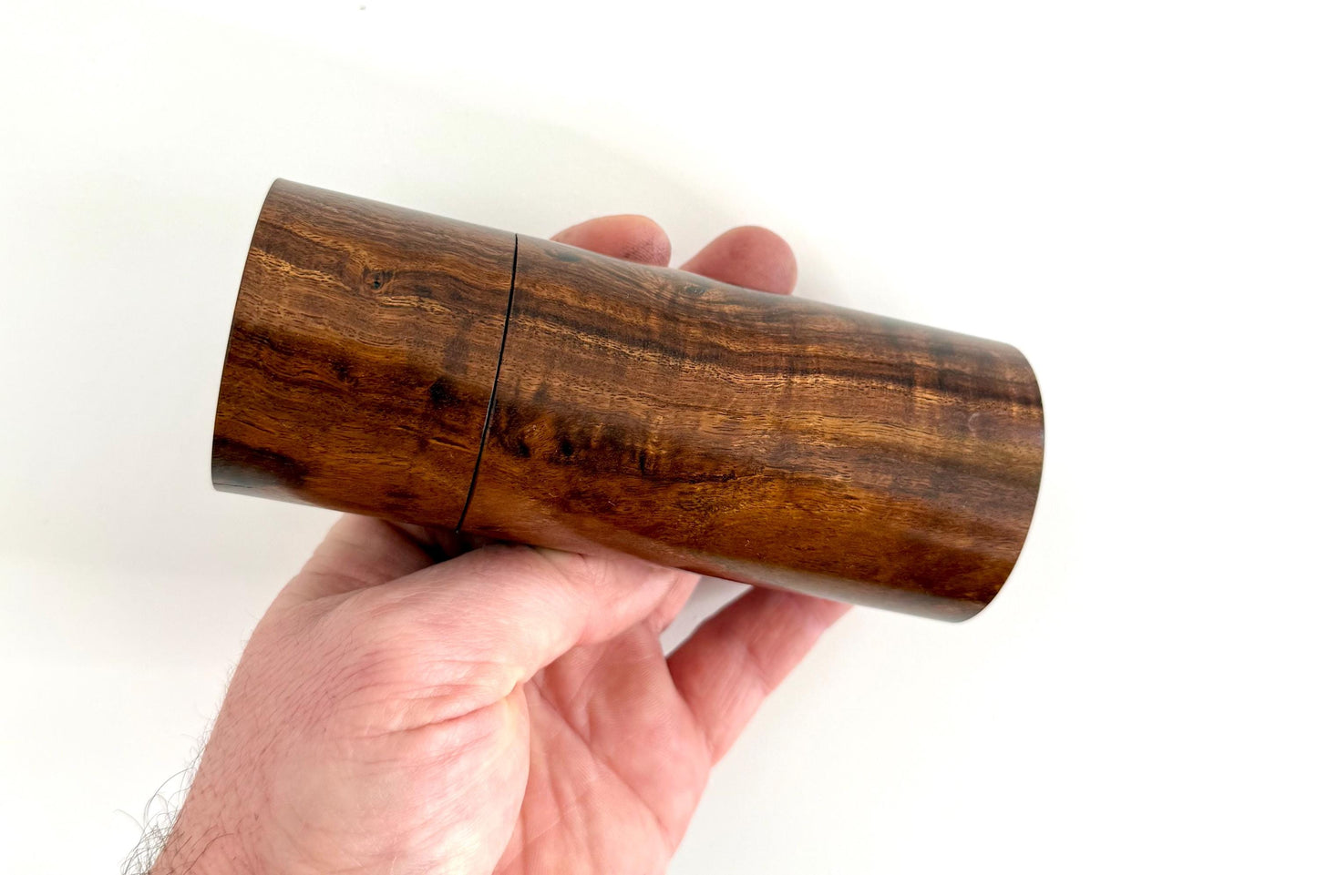 Mans hand holding single straight cylindrical Black Mulga timber grinder