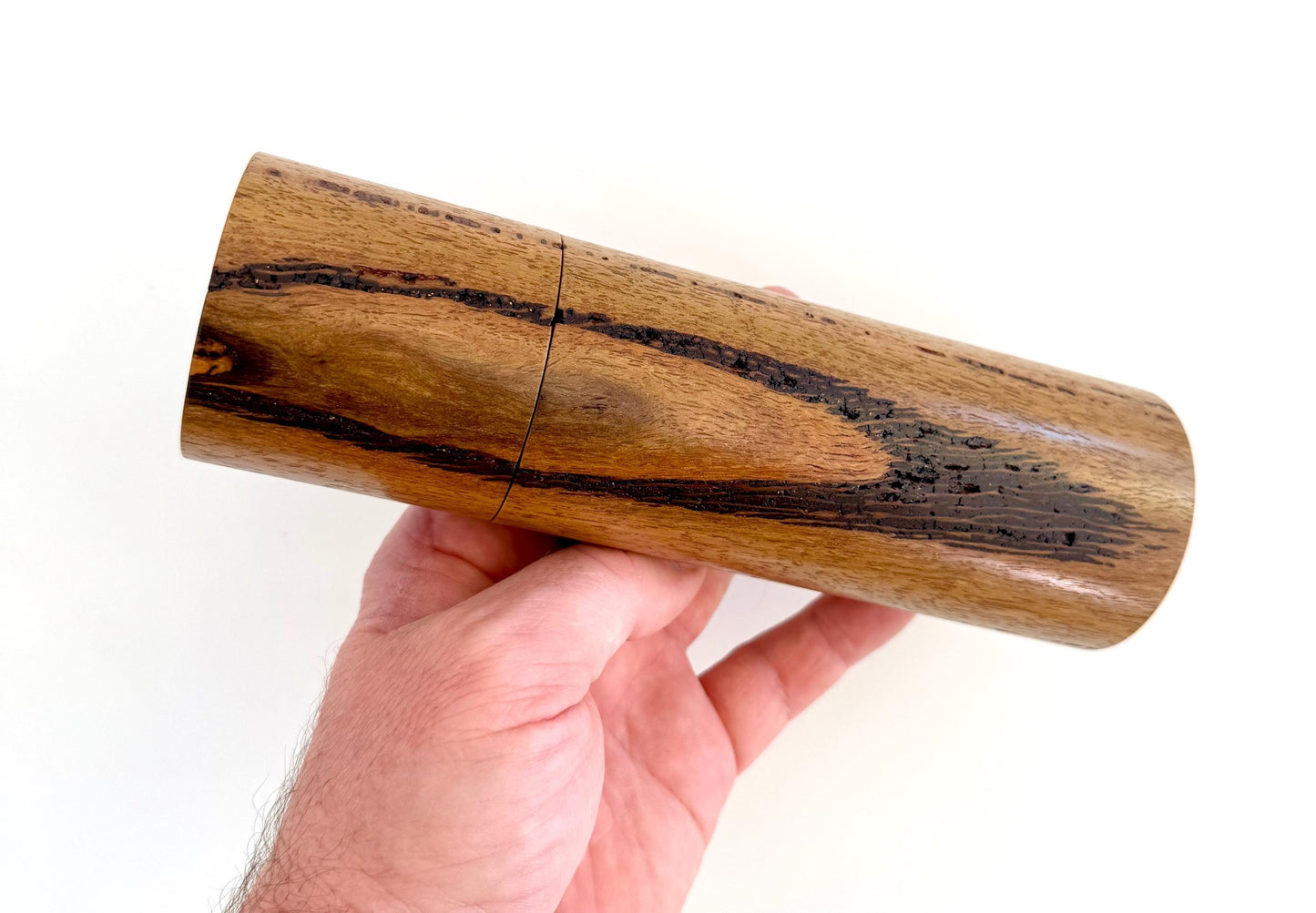 Mans hand holding single straight cylindrical Marri timber grinder