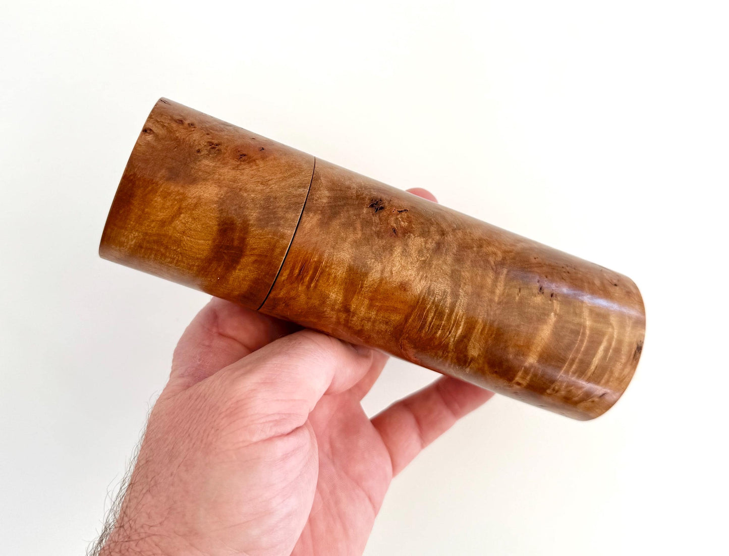 Mans hand holding single straight cylindrical Myrtle Burl timber grinder