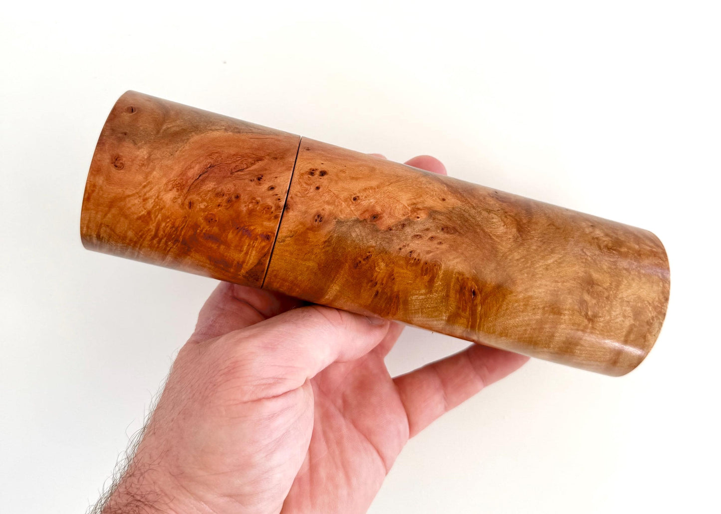 Mans hand holding single straight cylindrical Myrtle Burl timber grinder