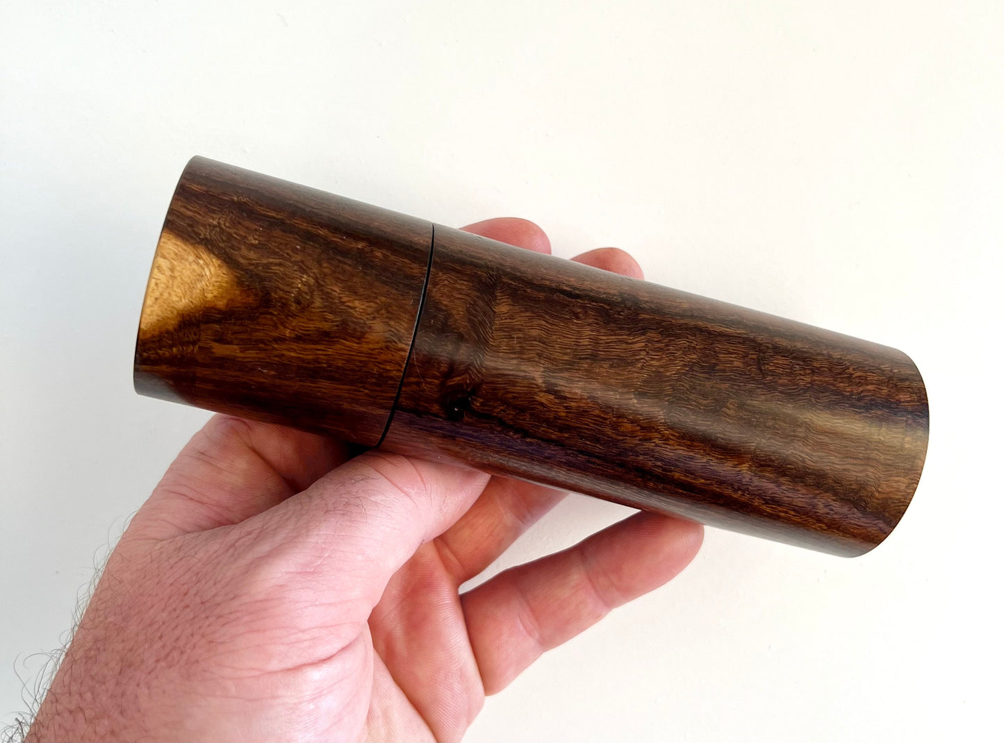 Mans hand holding single straight cylindrical Western Myall grinder