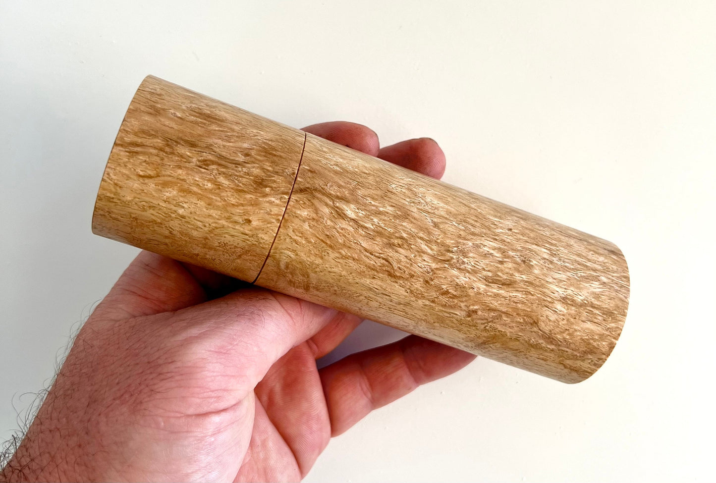 Mans hand holding single straight cylindrical Bluegum grinder