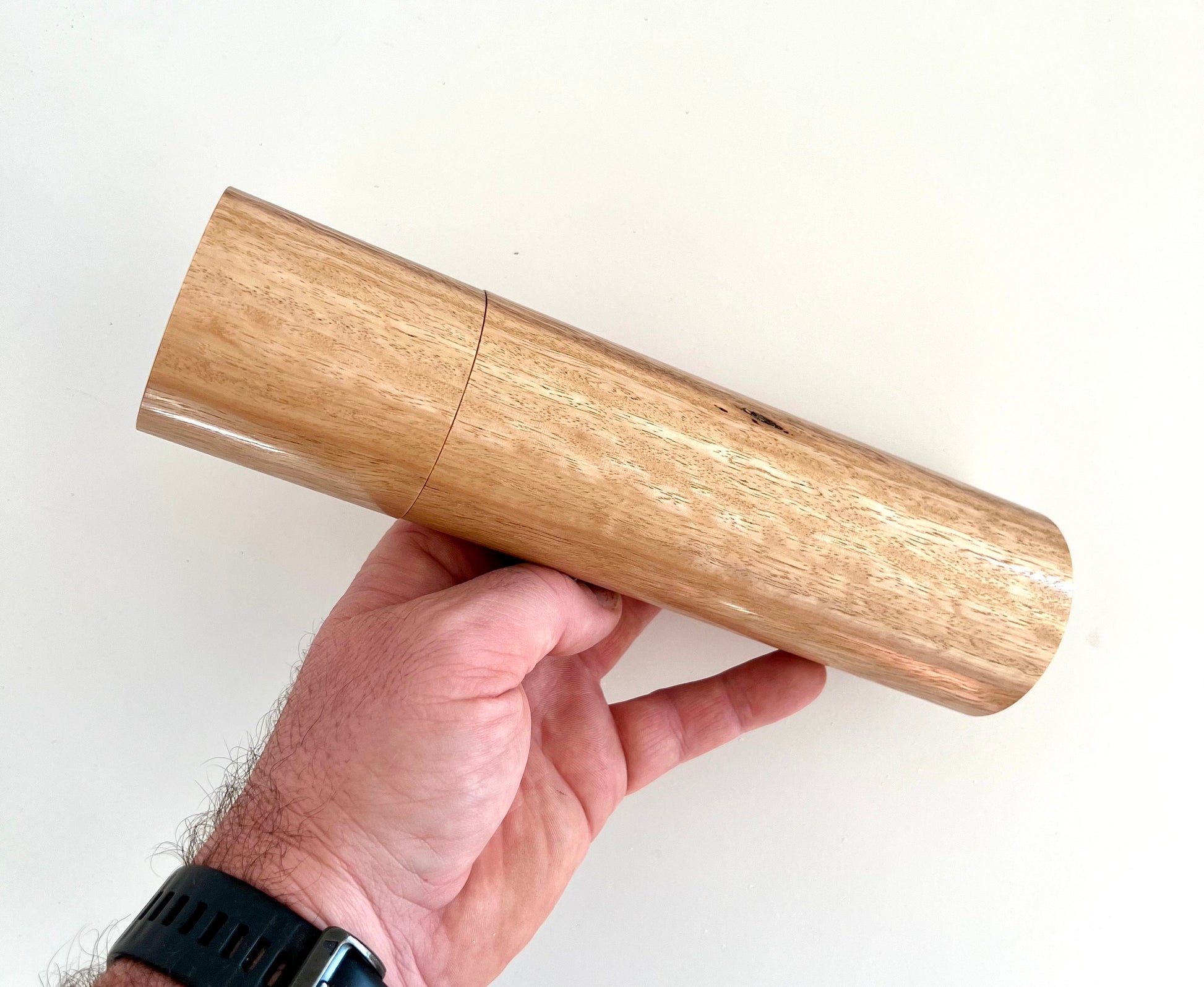 Mans hand holding single straight cylindrical Tasmanian blue gum timber grinder