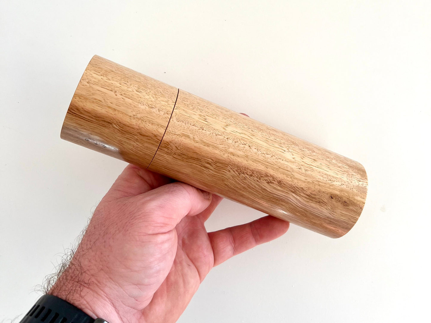 Mans hand holding single straight cylindrical Tasmanian blue gum timber grinder