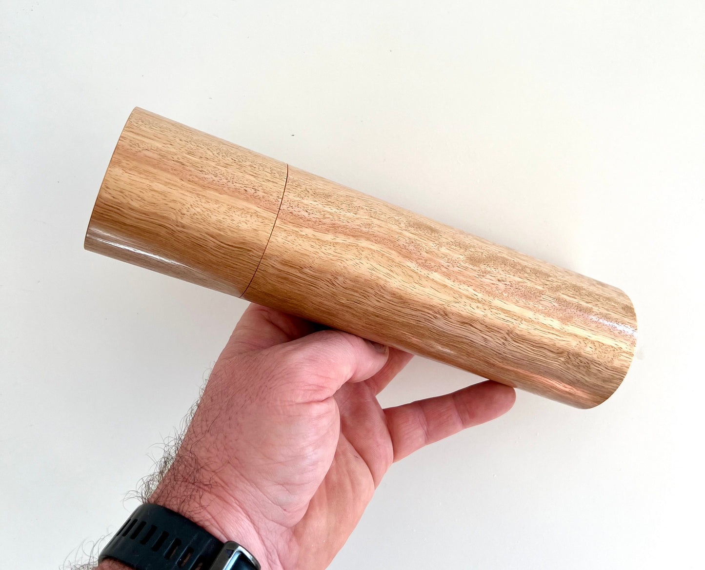 Mans hand holding single straight cylindrical Tasmanian blue gum timber grinder