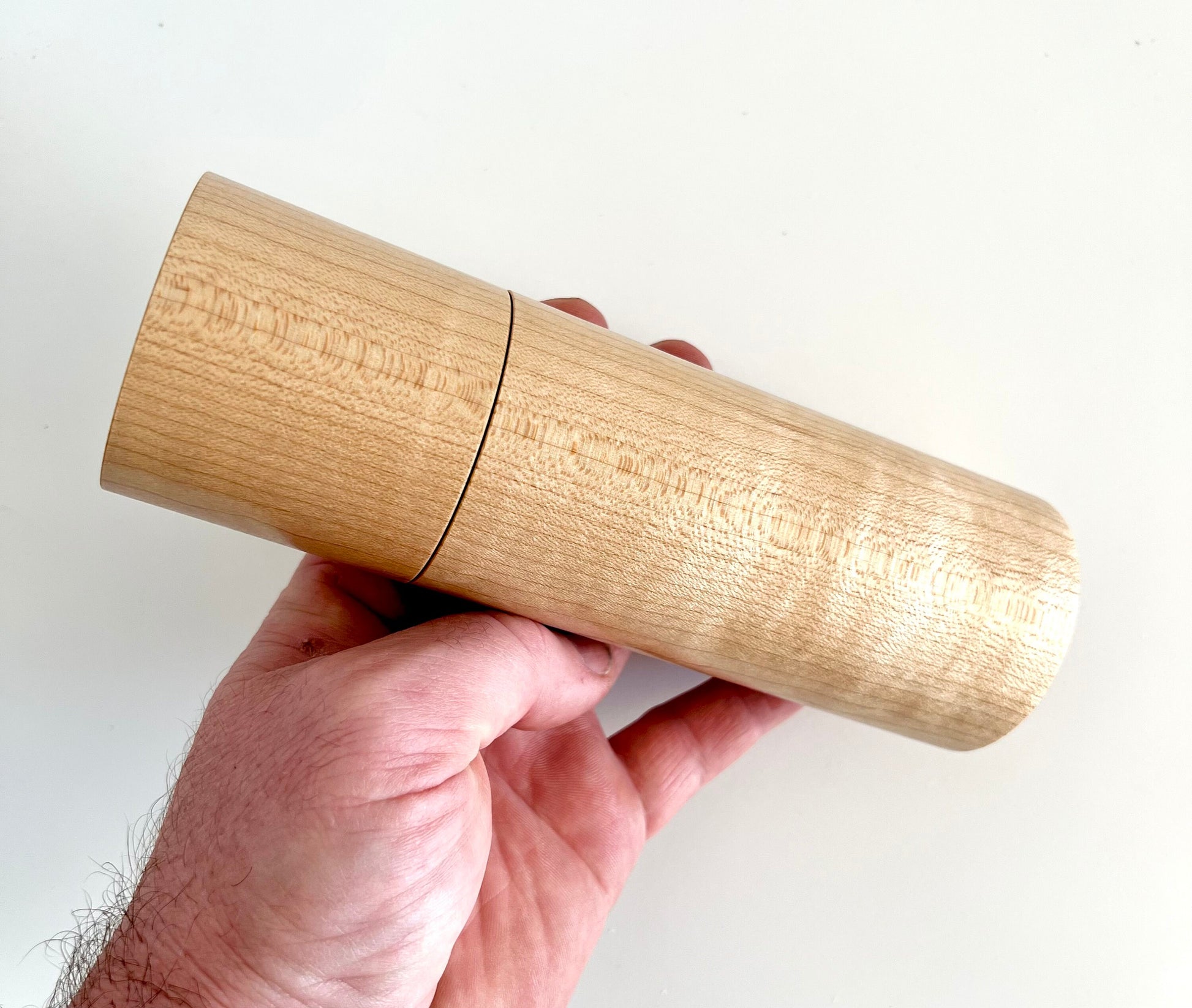 Mans hand holding single straight cylindrical Maple wood grinder