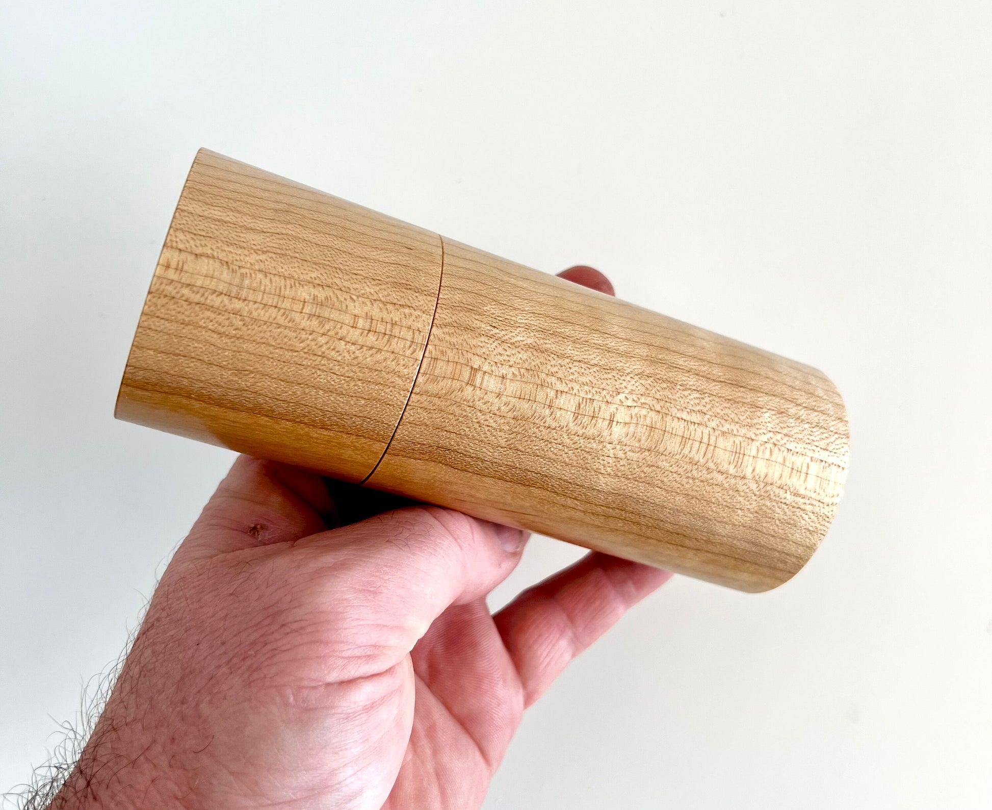 Mans hand holding single straight cylindrical Maple wood grinder