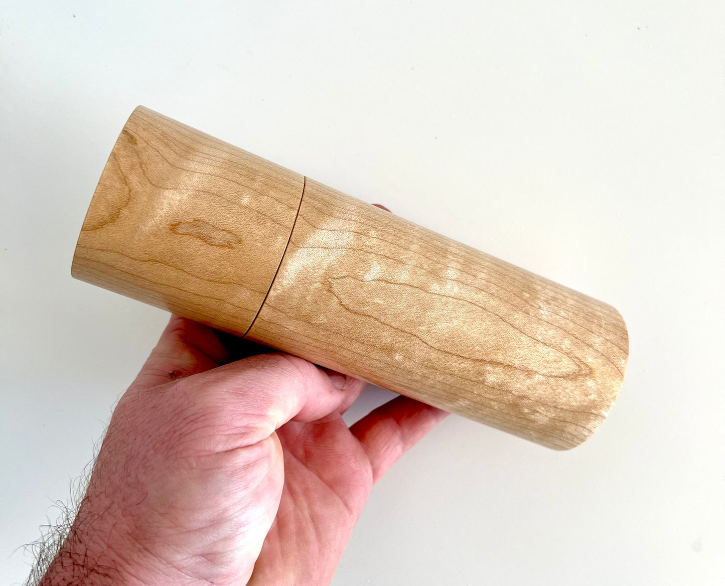 Mans hand holding single straight cylindrical Maple wood grinder