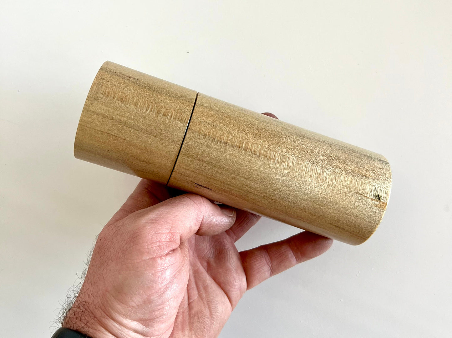 Mans hand holding single straight cylindrical Norfolk island pine grinder