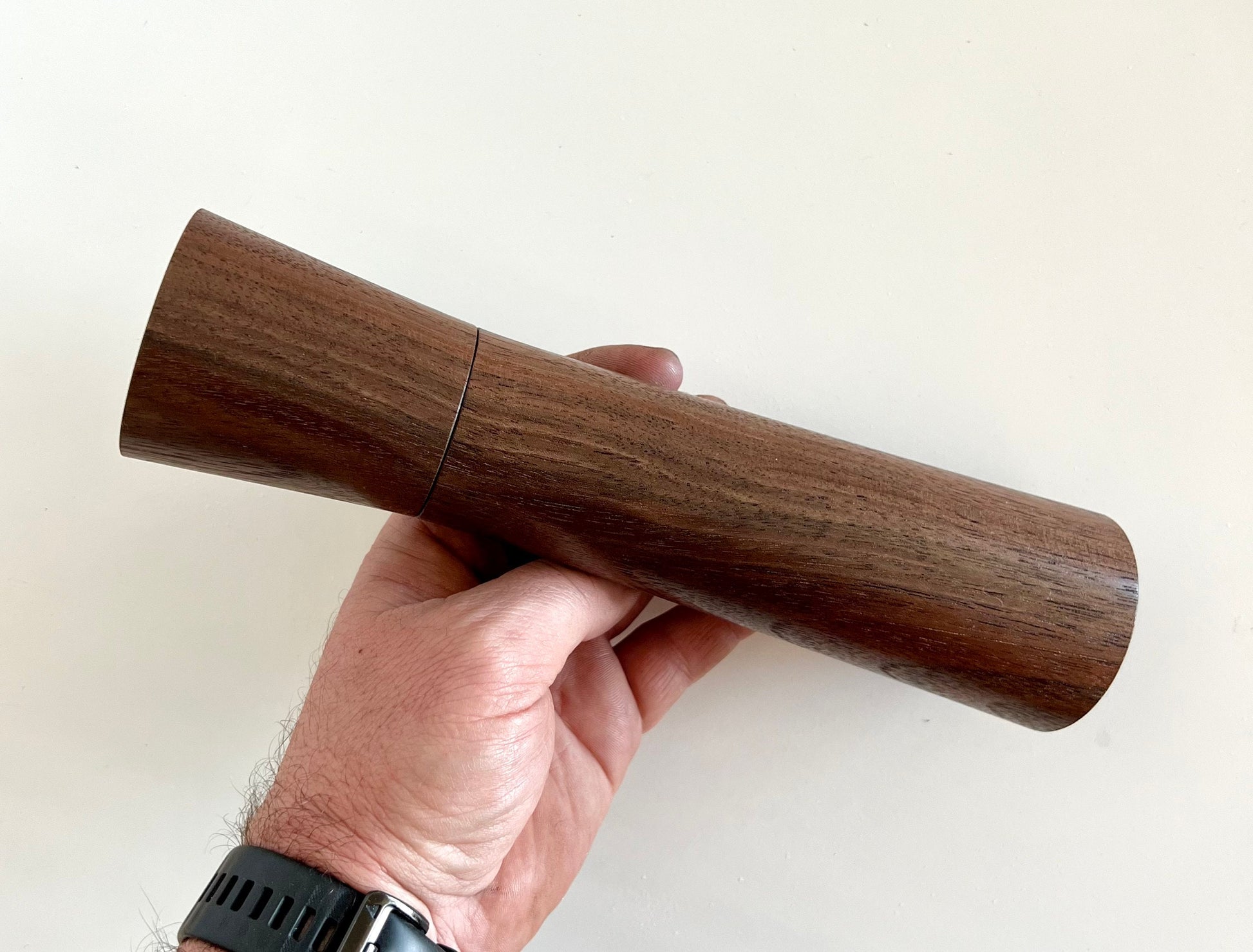 Mans hand holding single straight tapered Walnut grinder.