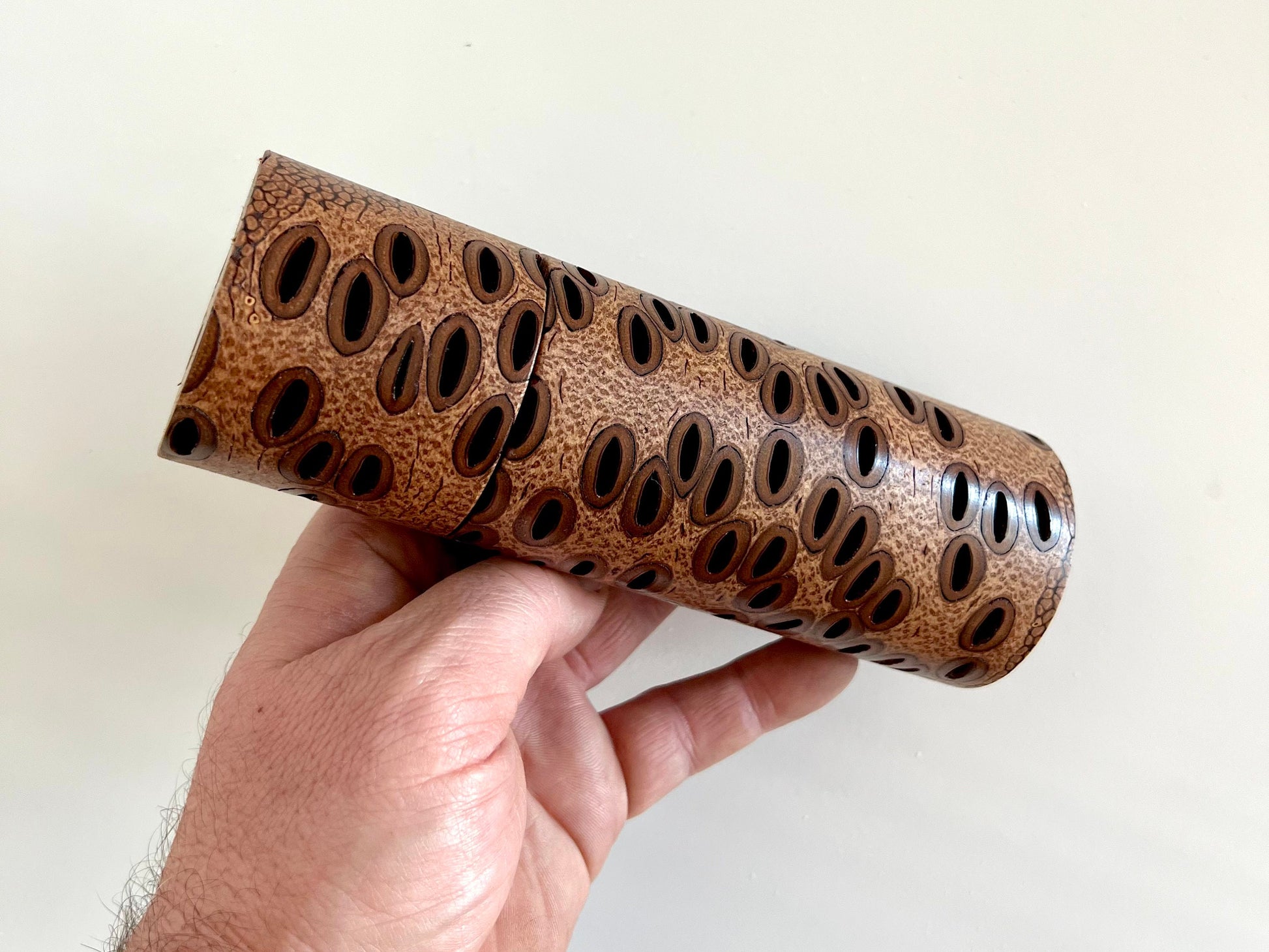 Mans hand holding single straight cylindrical Banksia seed pod grinder