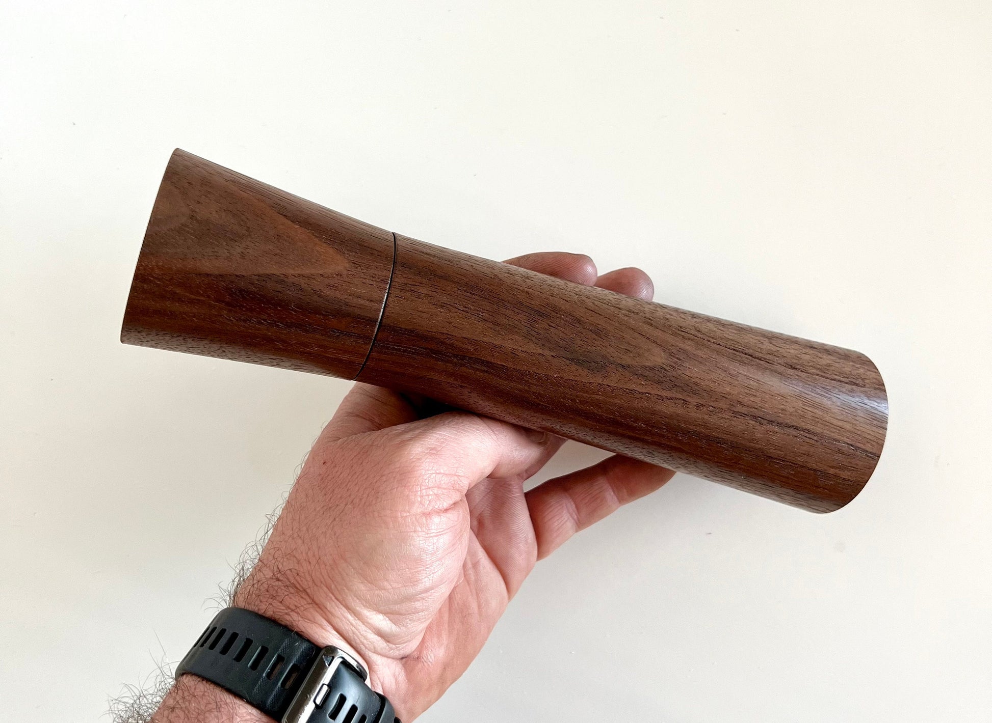 Mans hand holding single straight tapered Walnut grinder.