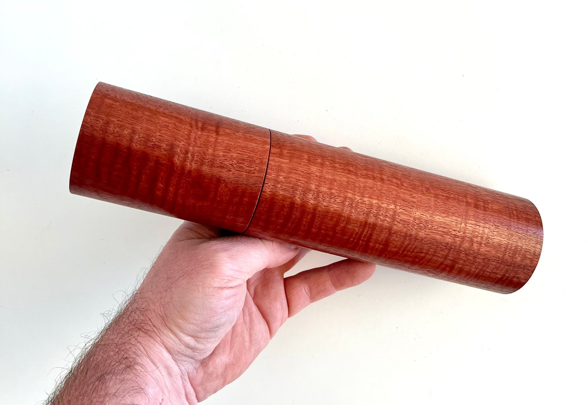 Mans hand holding single straight cylindrical Jarrah timber grinder