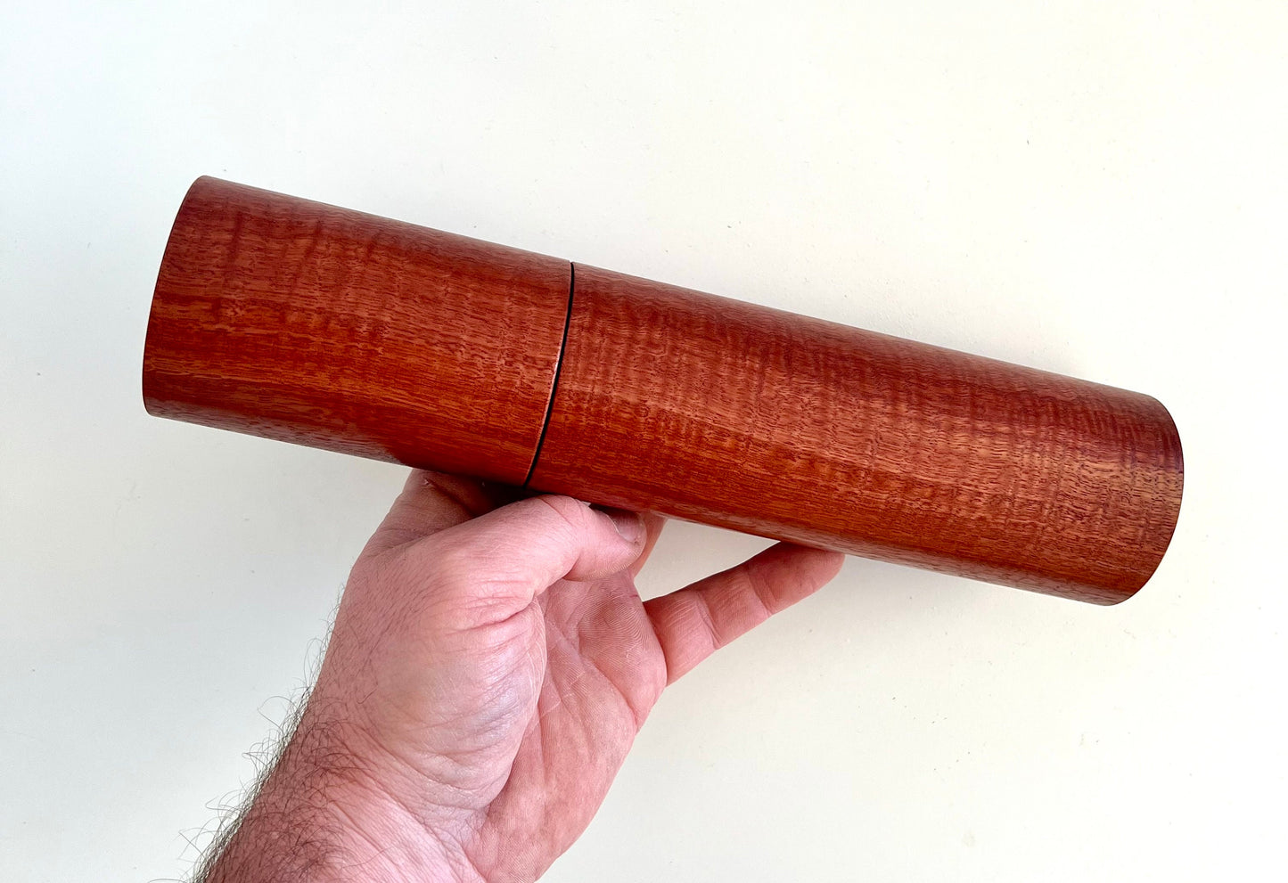 Mans hand holding single straight cylindrical Jarrah timber grinder