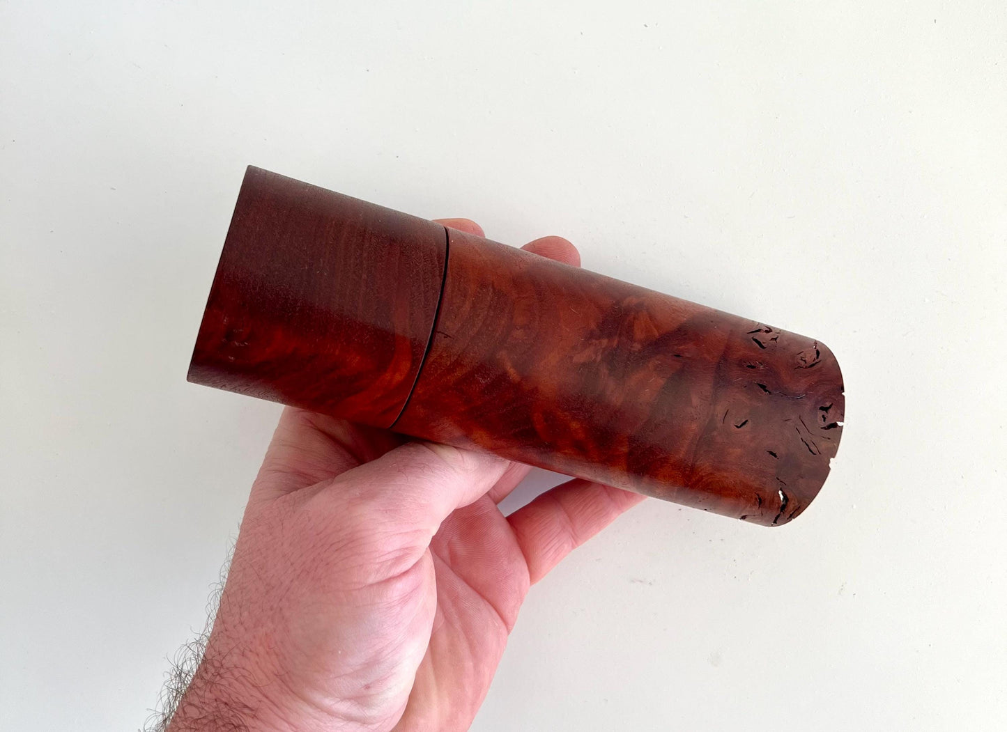 Mans hand holding single straight cylindrical Jarrah timber grinder