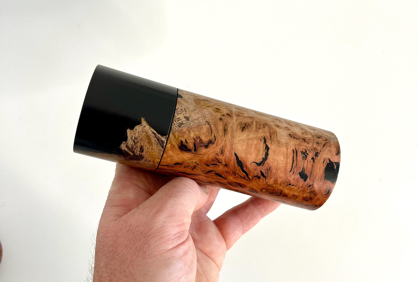 Mans hand holding single straight cylindrical Jarrah burl timber grinder