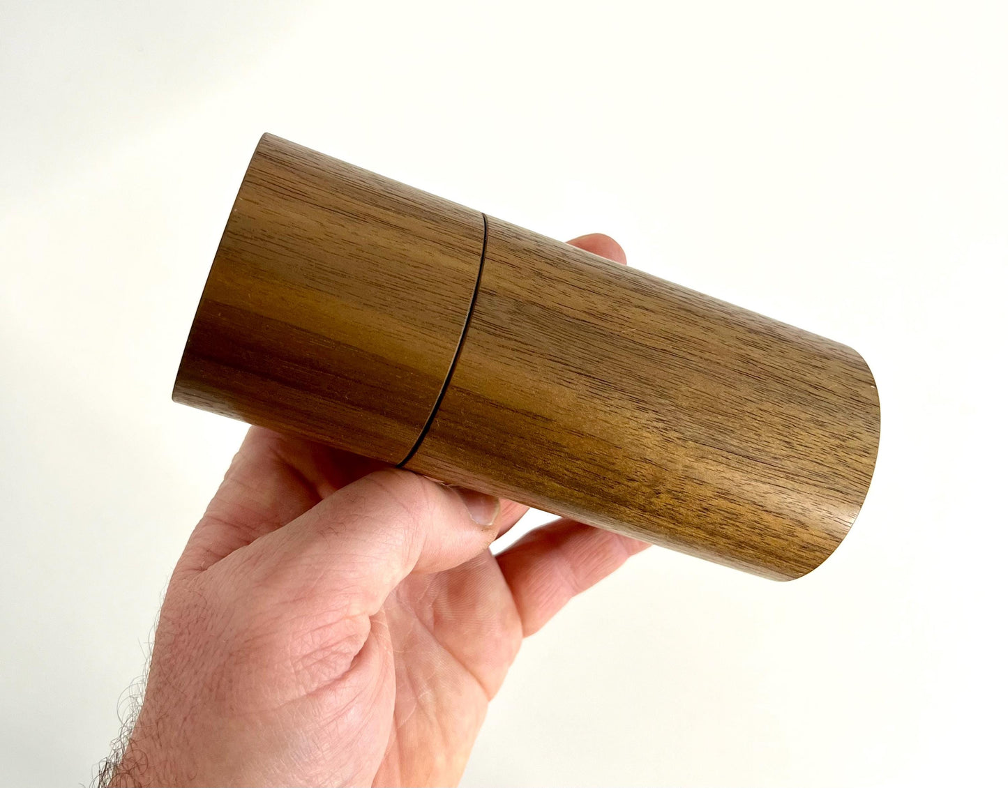 Mans hand holding single straight cylindrical Black Walnut timber grinder