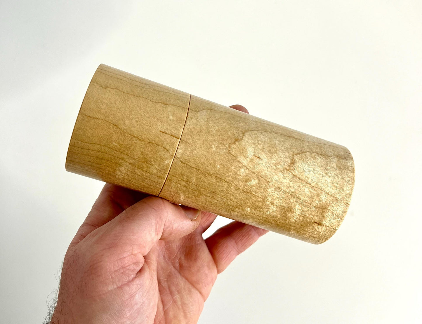 Mans hand holding single straight cylindrical Maple timber grinder