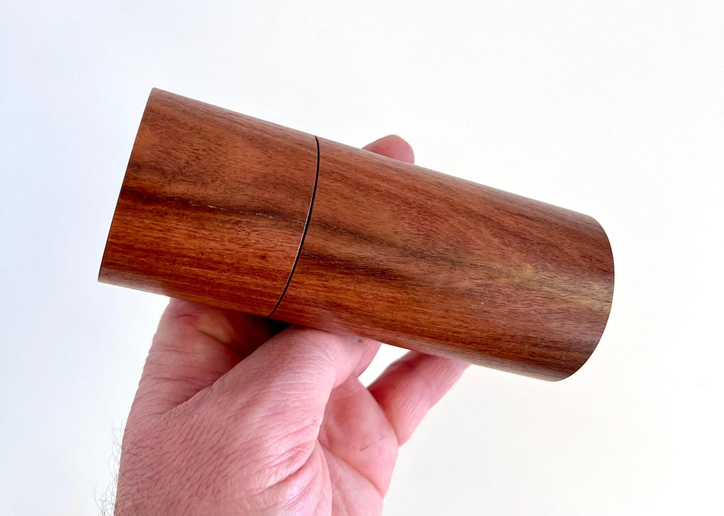 Mans hand holding single straight cylindrical Salmon gum timber grinder