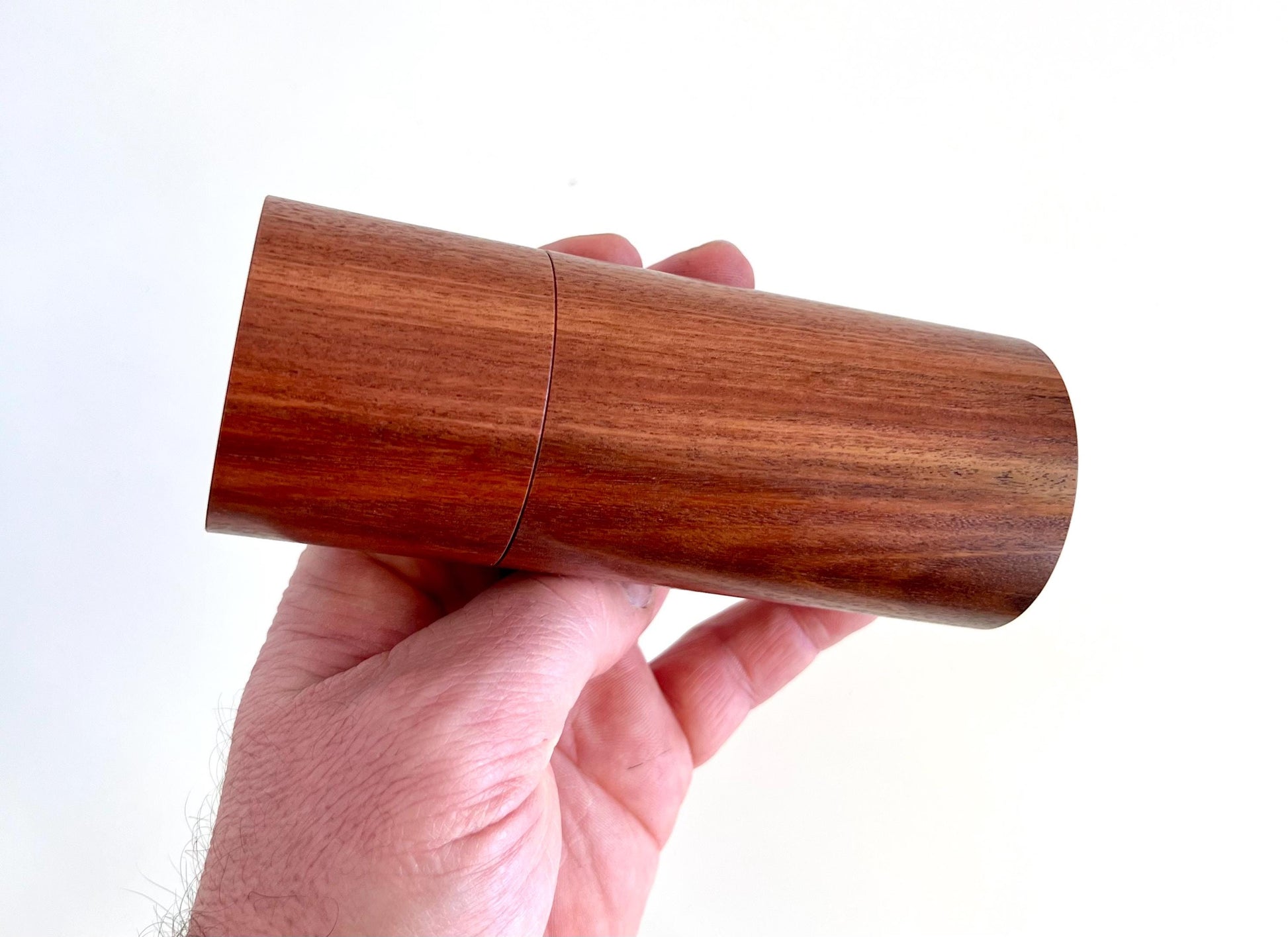 Mans hand holding single straight cylindrical Salmon gum timber grinder